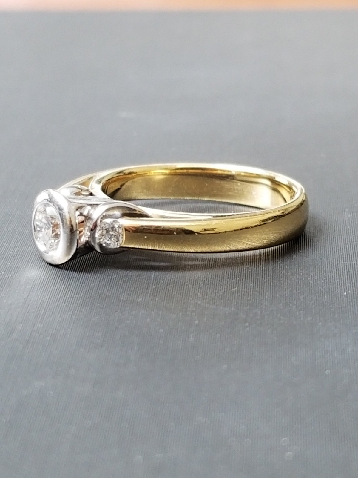Bezel set natural diamond trilogy ring in 18ct gold, angled view